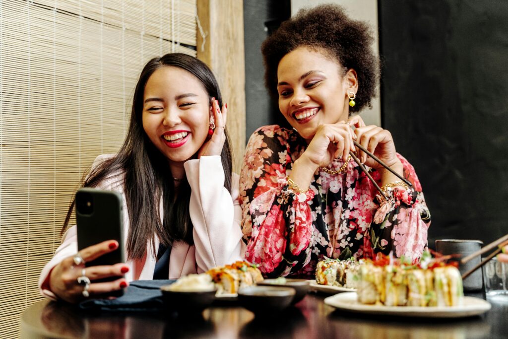Two women enjoying sushi while taking a selfie, creating memorable moments at a restaurant.